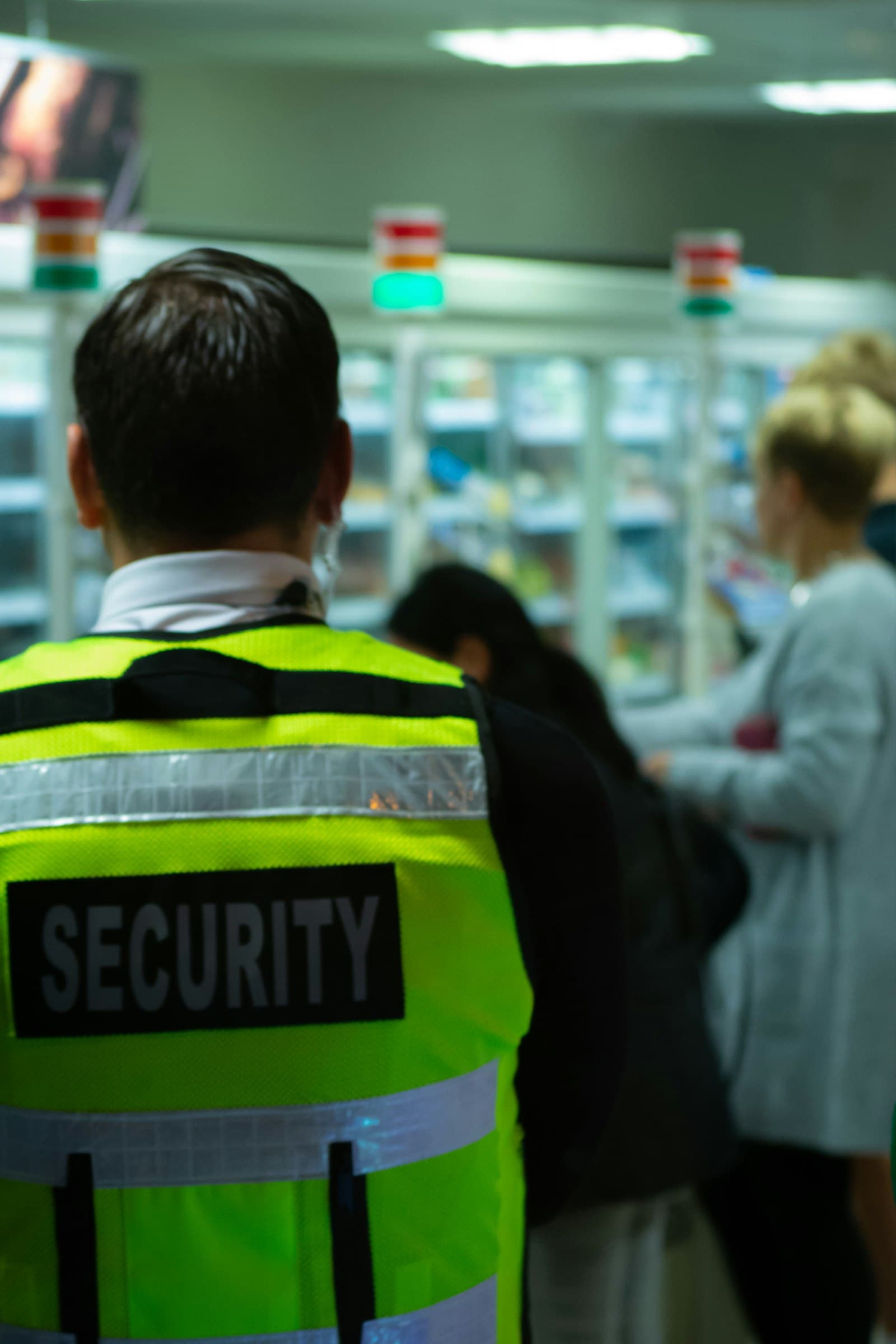 Beveiliger in signaalvest op de winkelvloer tussen klanten